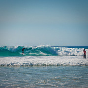 surfer ćwiczy manewr backside cutback, otrzymując instrukcje od trenera przez kask z radiem