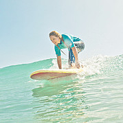 surfer wstaje na desce i łapie czystą, zieloną falę podczas lekcji surfingu